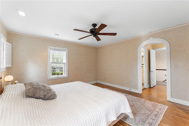 bedroom with light wood finished floors, ornamental molding, baseboards, arched walkways, and a ceiling fan