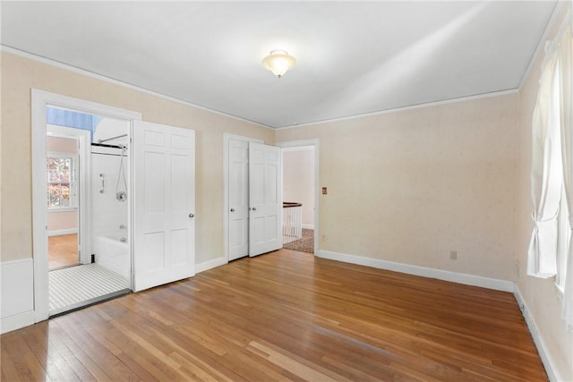 unfurnished bedroom featuring hardwood / wood-style flooring, multiple windows, crown molding, and baseboards
