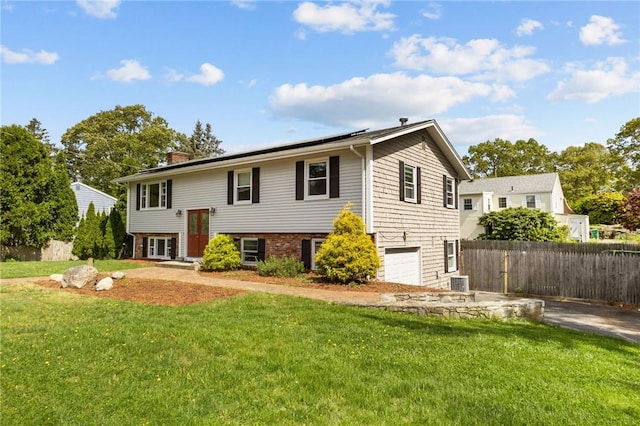 bi-level home featuring a garage, solar panels, a chimney, cooling unit, and driveway