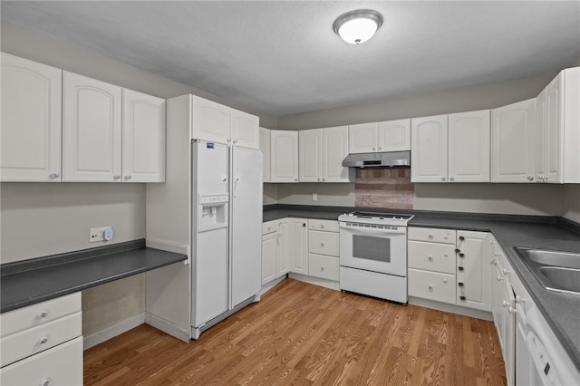 kitchen featuring white appliances, under cabinet range hood, dark countertops, light wood-style flooring, and white cabinets