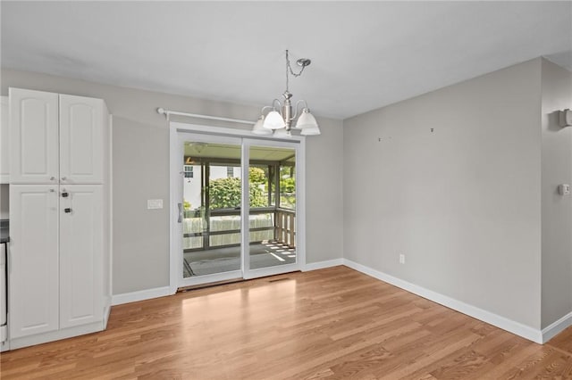 unfurnished dining area featuring baseboards, light wood-style flooring, and a chandelier