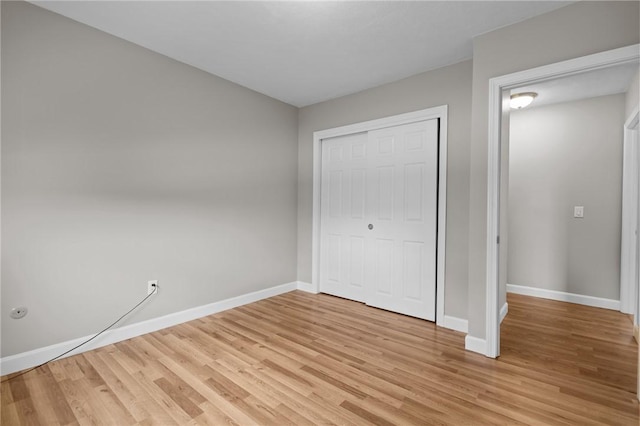 unfurnished bedroom featuring baseboards, light wood finished floors, and a closet