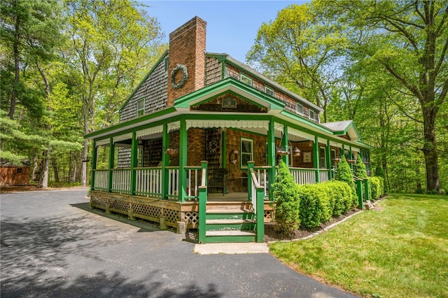 view of front of home with a porch, a chimney, driveway, and a front lawn