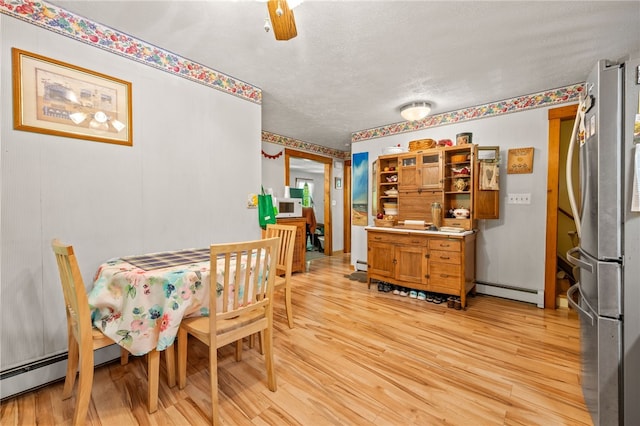 dining space with a baseboard heating unit, light wood finished floors, and a textured ceiling