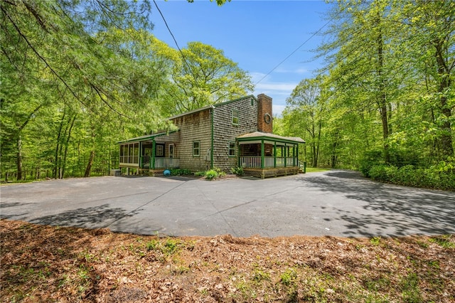 view of side of home with a chimney, a sunroom, and a porch