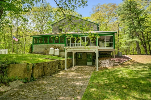 rear view of house with a sunroom, decorative driveway, central AC unit, and a yard
