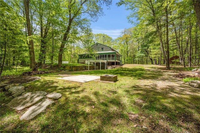 view of grassy yard with an outdoor fire pit, a patio, a wooden deck, and a view of trees