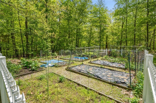 view of yard with a vegetable garden, a wooded view, and fence