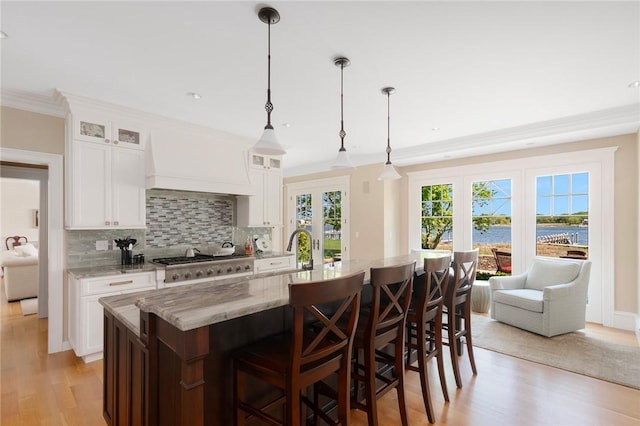 136 Adams Point Rd, Barrington, RI 02806 - kitchen featuring light wood finished floors, tasteful backsplash, light stone counters, glass insert cabinets, and ornamental molding