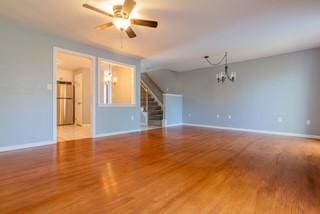 unfurnished living room with stairway, wood finished floors, baseboards, a chandelier, and a ceiling fan