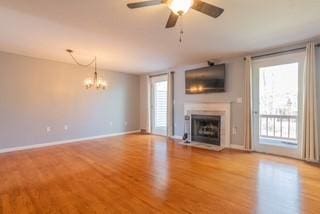 unfurnished living room with wood finished floors, a fireplace, a ceiling fan, a chandelier, and baseboards