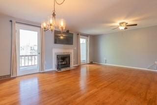 unfurnished living room featuring a fireplace with flush hearth, wood finished floors, a chandelier, ceiling fan, and baseboards