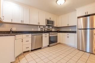 kitchen with stainless steel appliances, dark countertops, a sink, and white cabinets
