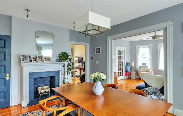 dining area with light wood finished floors, a fireplace with flush hearth, and ceiling fan