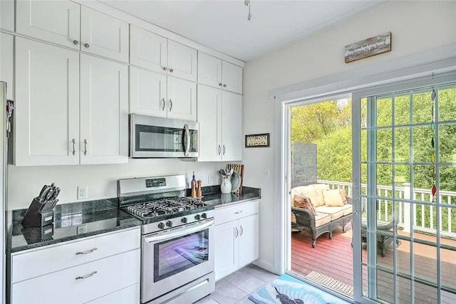 kitchen featuring appliances with stainless steel finishes, white cabinetry, dark stone counters, and light tile patterned floors