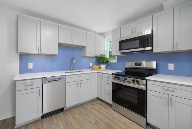 kitchen featuring stainless steel appliances, a sink, light wood-style floors, and light countertops