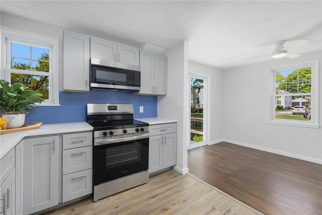 kitchen featuring appliances with stainless steel finishes, light wood finished floors, light countertops, gray cabinets, and healthy amount of natural light