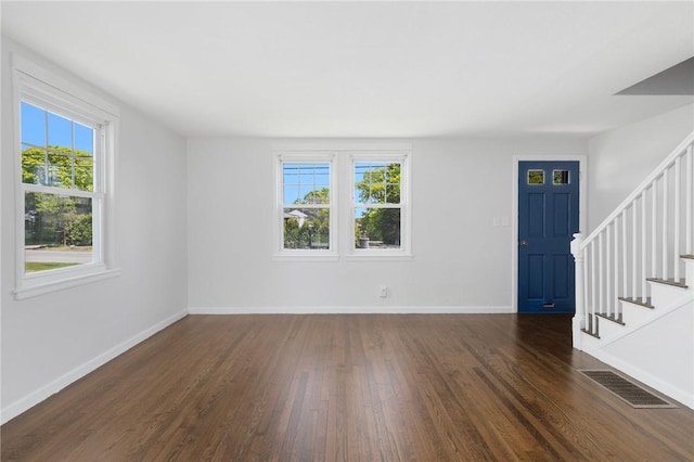 unfurnished living room with healthy amount of natural light, dark wood-style flooring, and stairs