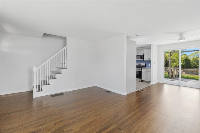 unfurnished living room with stairway, wood finished floors, baseboards, and a ceiling fan