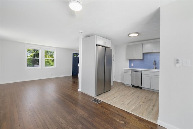 kitchen featuring appliances with stainless steel finishes, open floor plan, wood finished floors, baseboards, and light countertops