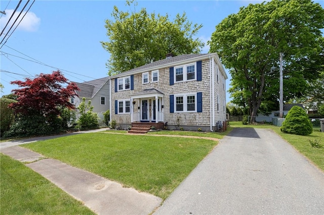 colonial house with a chimney, asphalt driveway, and a front lawn