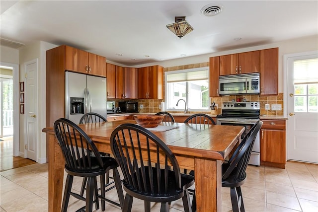 103 Carrs Pond Rd, West Greenwich, RI 02817 - kitchen with stainless steel appliances, light tile patterned flooring, backsplash, and brown cabinetry