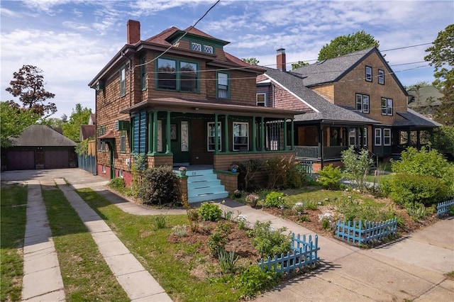 view of front of home with a chimney, a porch, an outdoor structure, a detached garage, and a shingled roof