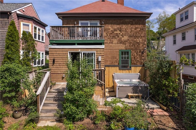 rear view of house featuring a hot tub, a balcony, a chimney, and fence