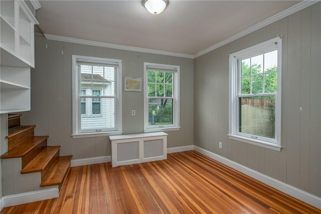 empty room with wood-type flooring, baseboards, ornamental molding, and stairway