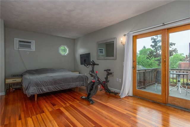 bedroom with a wall mounted air conditioner, wood-type flooring, access to exterior, and baseboards