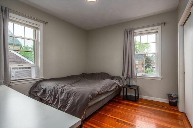 bedroom with cooling unit, wood finished floors, and baseboards