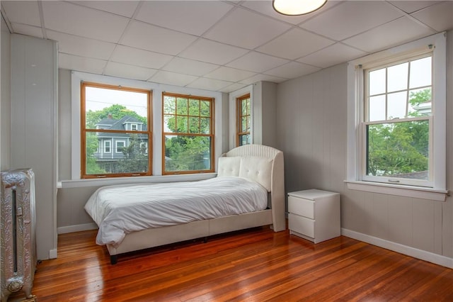 bedroom with hardwood / wood-style flooring, a paneled ceiling, and baseboards