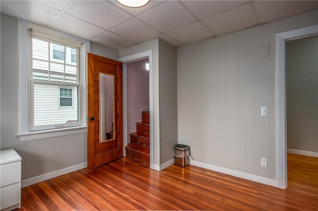 empty room featuring wood finished floors, baseboards, stairs, and a drop ceiling