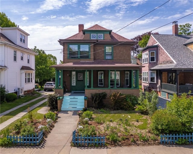 american foursquare style home with covered porch, fence, a chimney, and roof with shingles