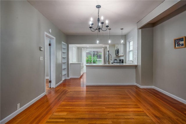 unfurnished dining area with wood finished floors, a chandelier, and baseboards