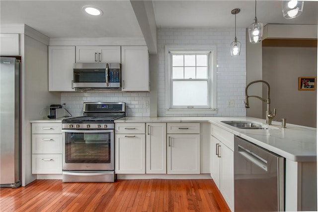 kitchen featuring stainless steel appliances, a sink, light countertops, a peninsula, and light wood-style flooring