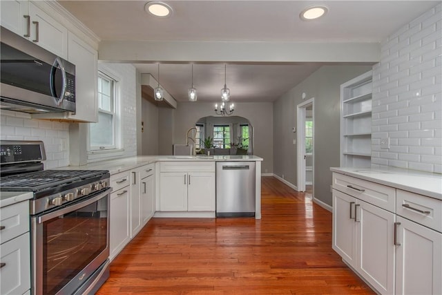kitchen featuring appliances with stainless steel finishes, a sink, a peninsula, backsplash, and light wood-style floors