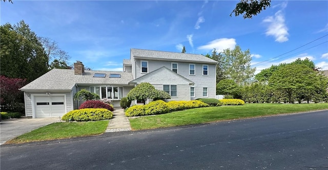 traditional home featuring a garage, concrete driveway, a front yard, and a chimney