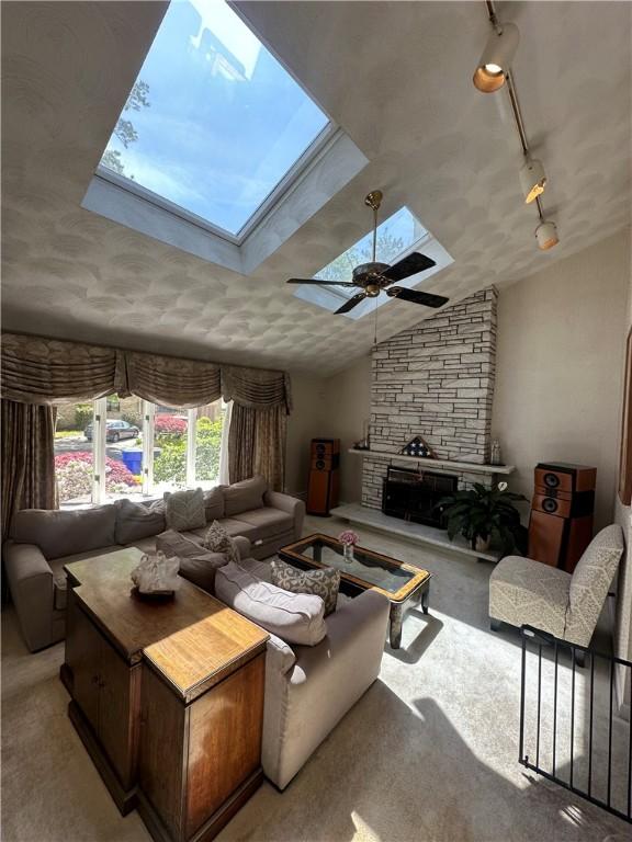 carpeted living area with a skylight, a stone fireplace, lofted ceiling, and ceiling fan