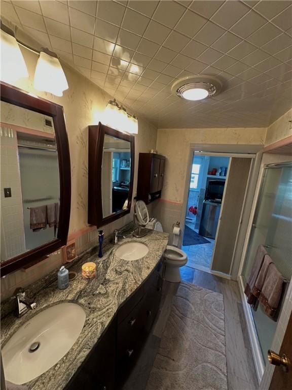 bathroom with a stall shower, double vanity, wood finished floors, and toilet