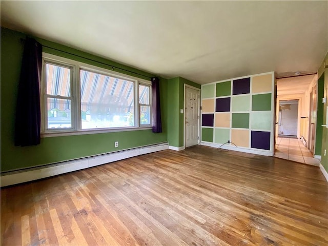 spare room with baseboard heating, hardwood / wood-style floors, and baseboards