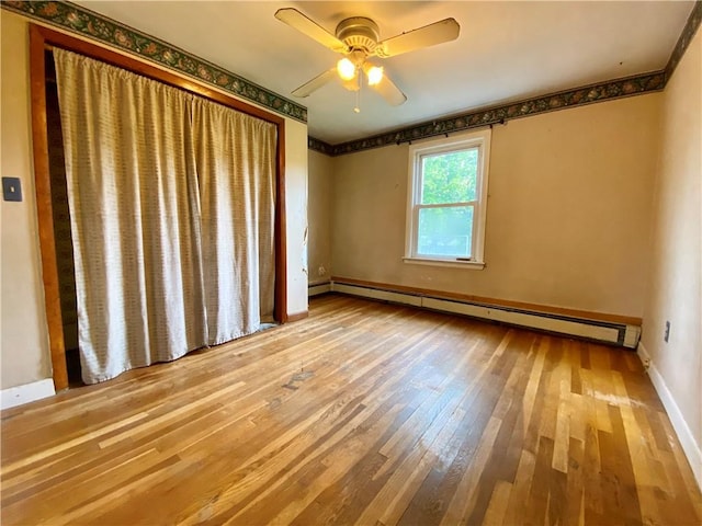 spare room featuring a baseboard radiator, hardwood / wood-style floors, ceiling fan, and baseboards