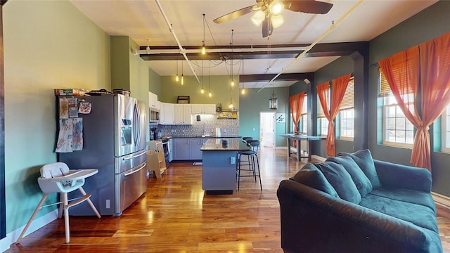 kitchen with stainless steel appliances, open floor plan, a kitchen bar, wood finished floors, and a ceiling fan