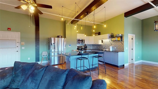 kitchen with stainless steel appliances, dark countertops, open floor plan, white cabinetry, and backsplash