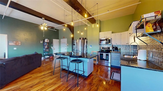 kitchen featuring appliances with stainless steel finishes, a sink, open floor plan, a breakfast bar area, and dark wood-type flooring
