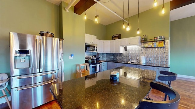 kitchen with stainless steel appliances, a towering ceiling, white cabinetry, backsplash, and pendant lighting