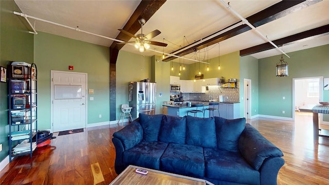 living area featuring wood finished floors, ceiling fan, baseboards, a towering ceiling, and beamed ceiling