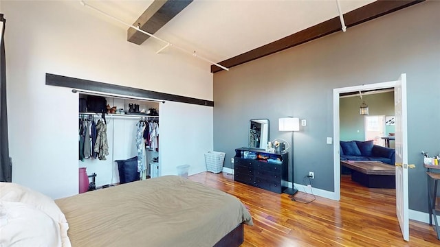 bedroom with wood finished floors, a closet, baseboards, and beam ceiling