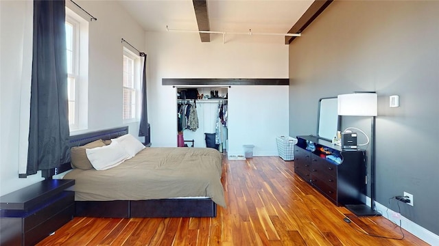 bedroom with wood finished floors, beamed ceiling, and a closet