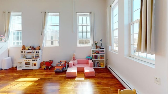 game room with wood finished floors, a high ceiling, a baseboard radiator, and baseboards